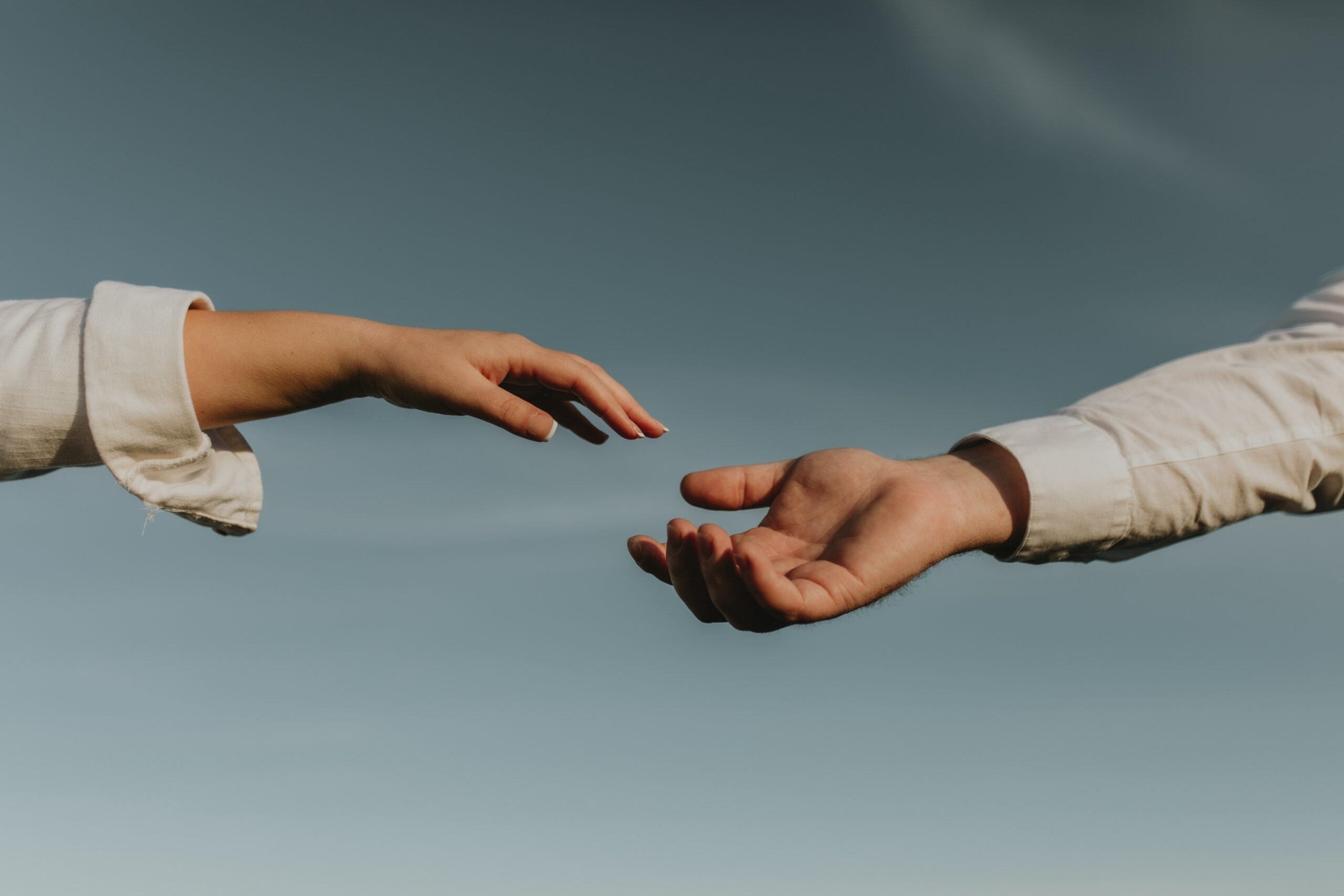 Two hands reaching out to each other against a blue sky to represent drug addiction rehab in long beach california.