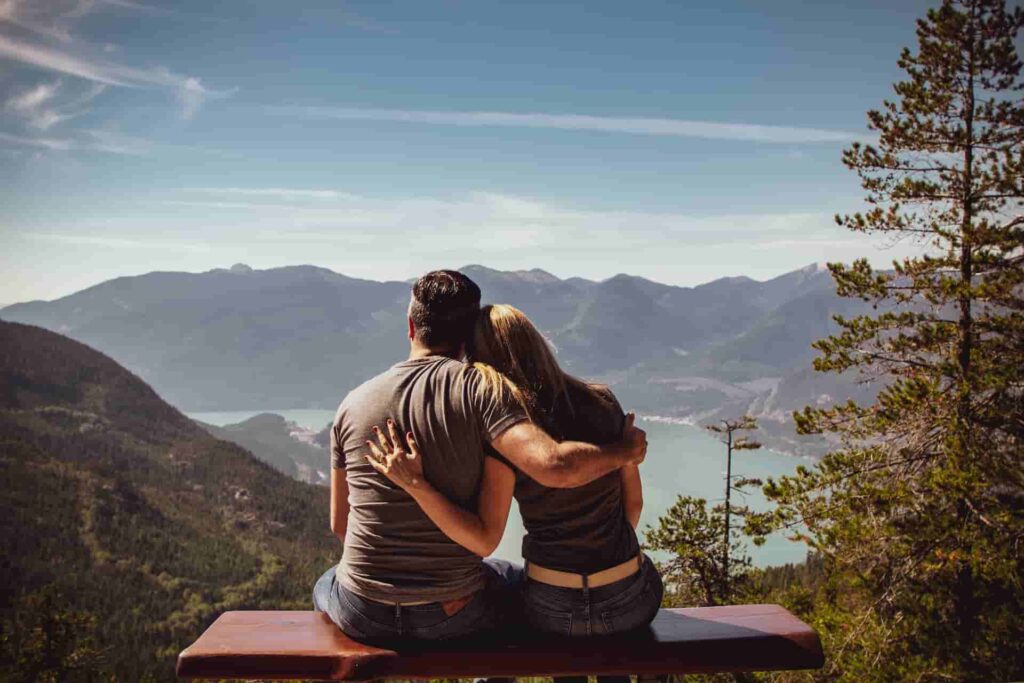 An image of a man and a woman, hugging, as they stare off at the lake