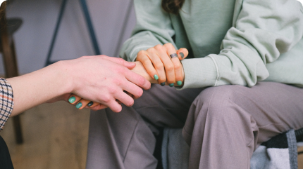 Two men sit with their hand on top of each other, presumably during an intervention where one of them is helping a family member recover from addiction.