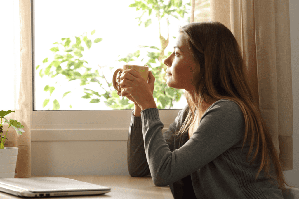 a woman is looking out a window while drinking coffee to represent alcohol stimulant effects.