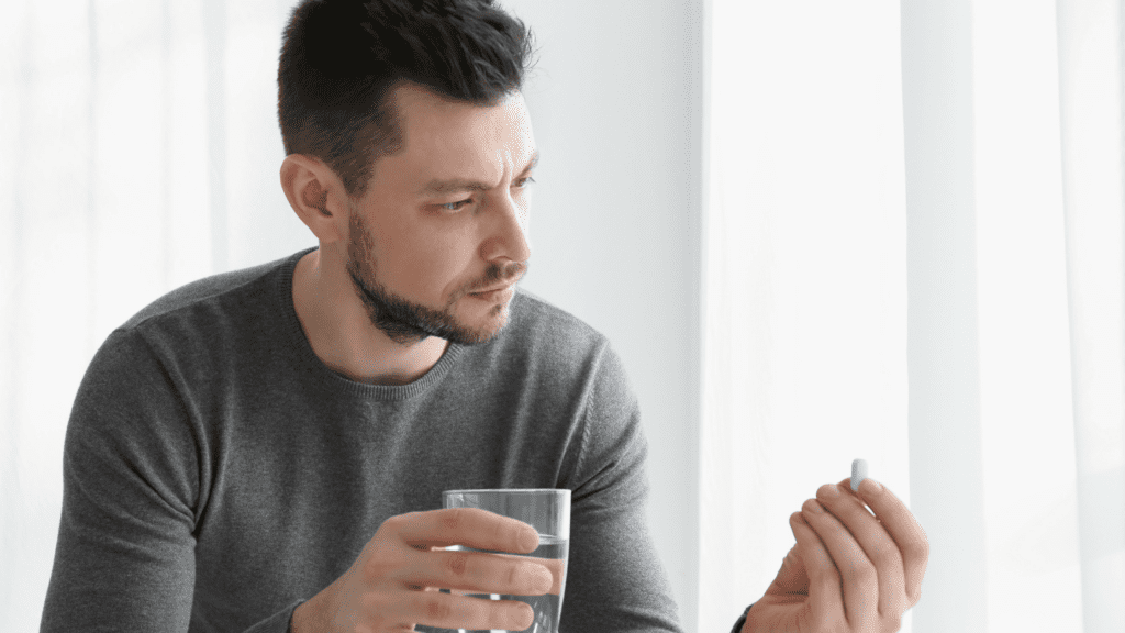 a man hold a drink in his hand and a pill to represent oxycodone and alcohol.