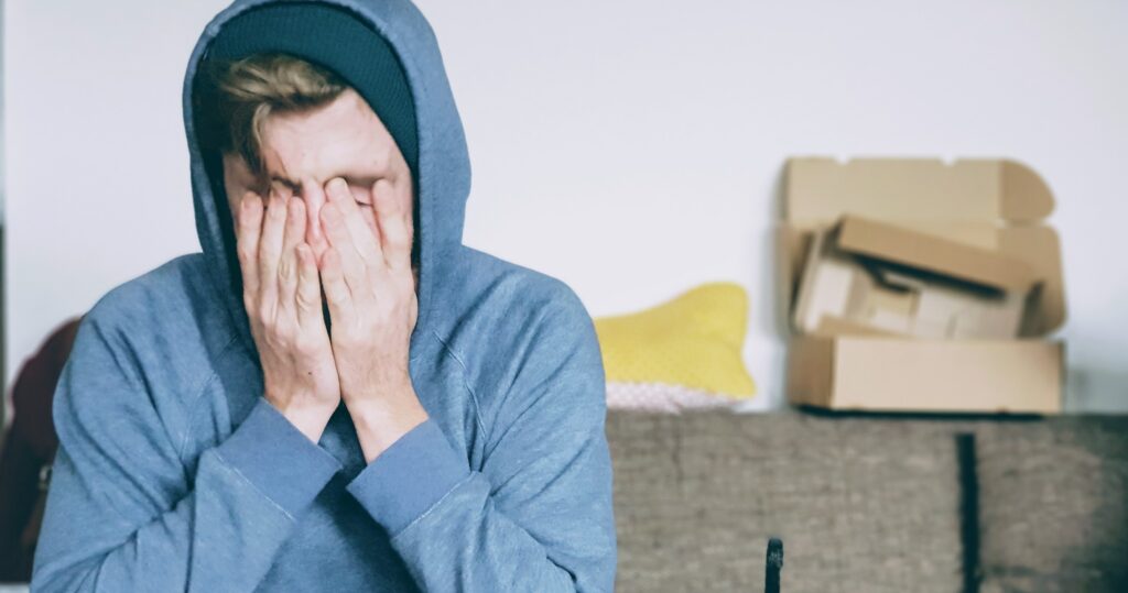 A young man sits with his hands rubbing his face to represent how long alcohol withdrawal lasts.