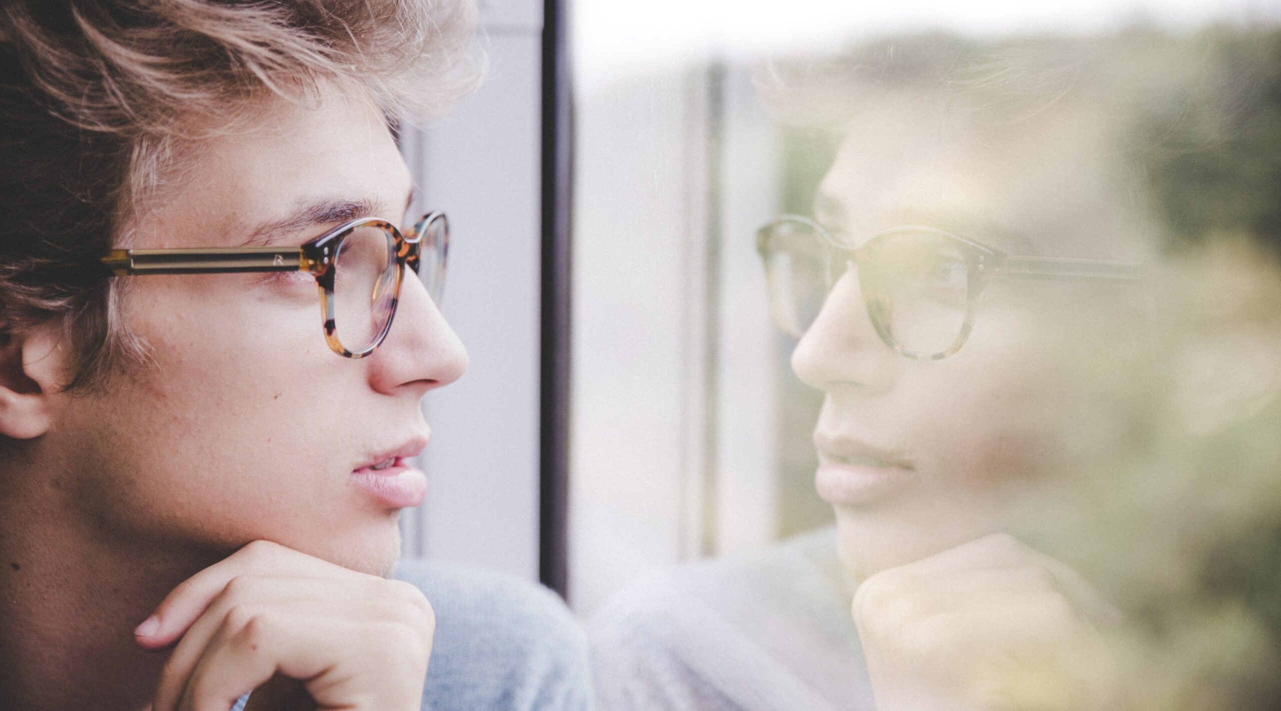 a man sits looking out a window to represent the dangers of mixing oxycodone and alcohol.