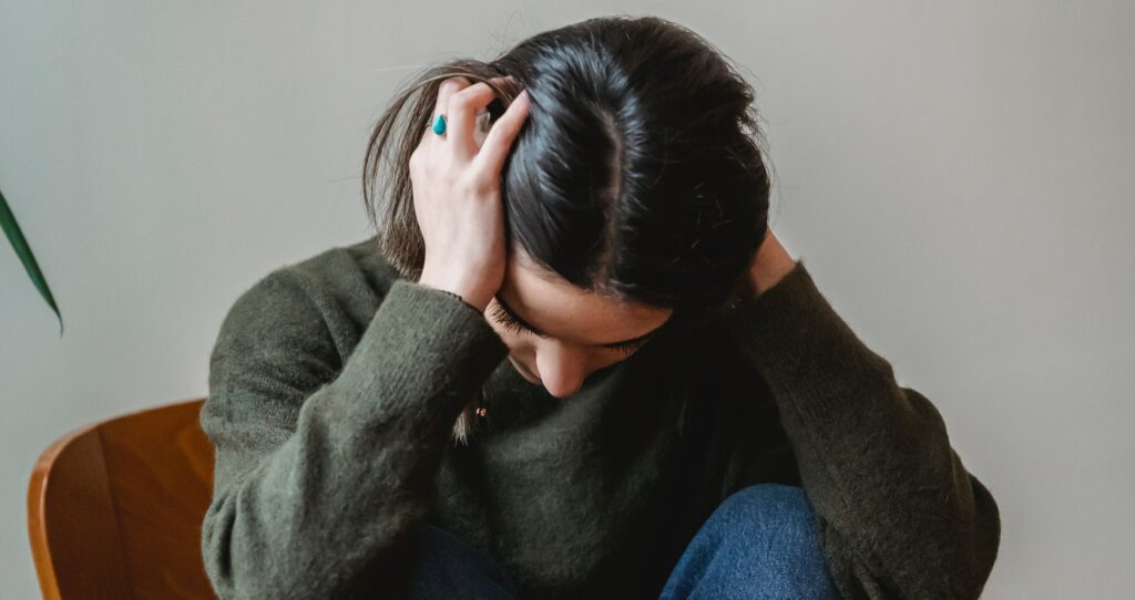 a woman sits with her head in her hands to represent opiate withdrawal.