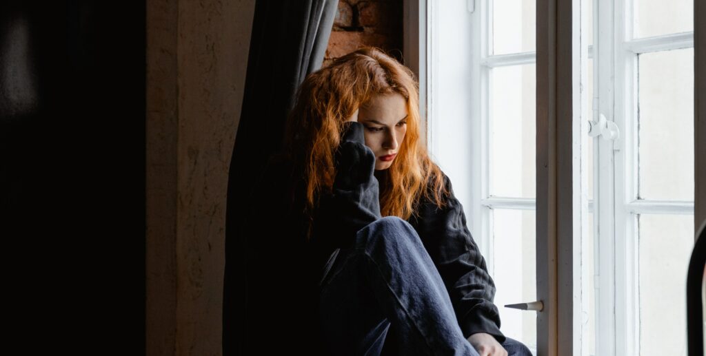 A woman sits at a window with her hand on her hair to represent the question, "how long does meth stay in your system?".