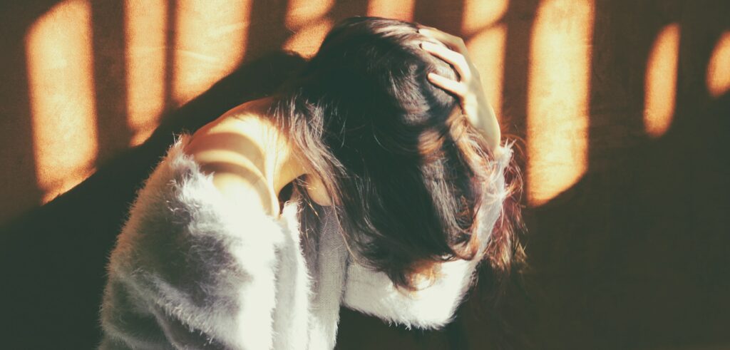 A woman sits by a window with her head down to represent how to treat heroin addiction.