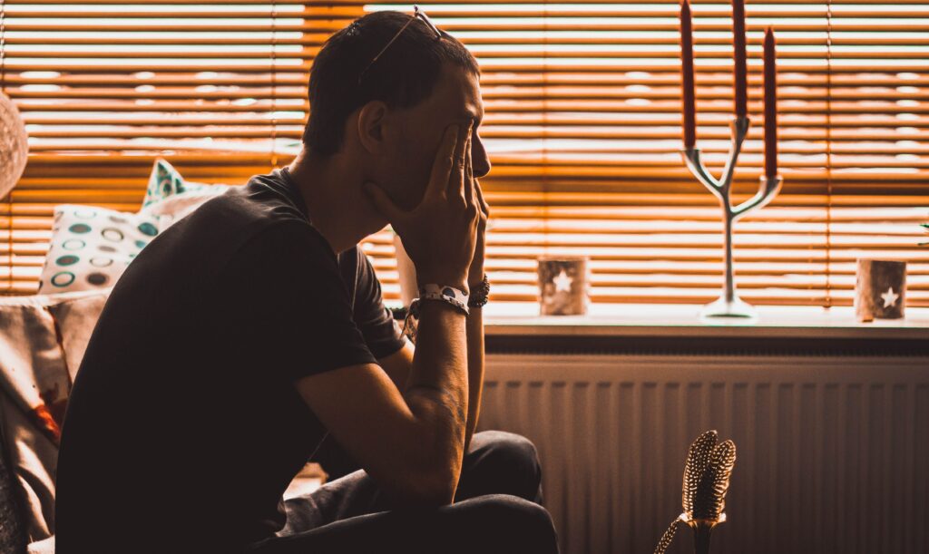 Man sitting down with head in hands to represent woman looking out at a sunset to represent adderall withdrawal symptoms