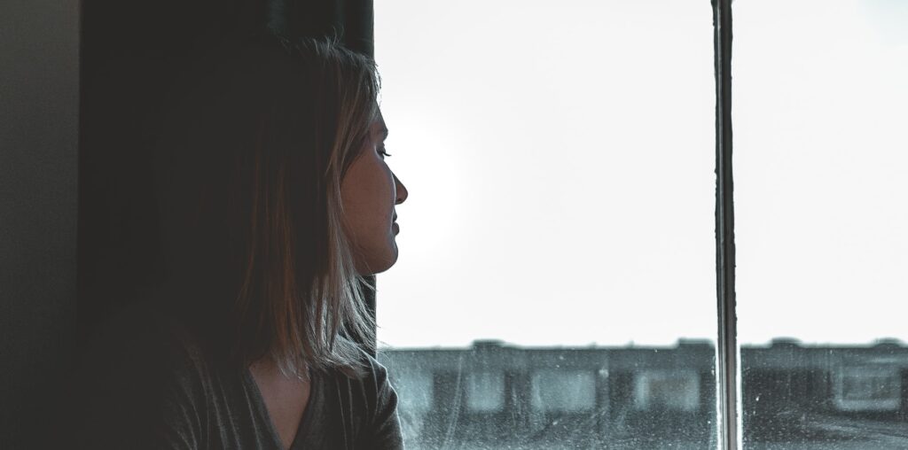 A woman looks out a window to represent how long is inpatient rehab.