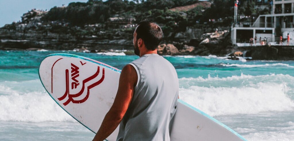 A man carries a surfboard representing mental health benefits of surfing.