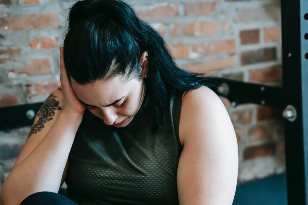 AN image of a woman looking down with her hand on her head, depicting symptoms of wet brain