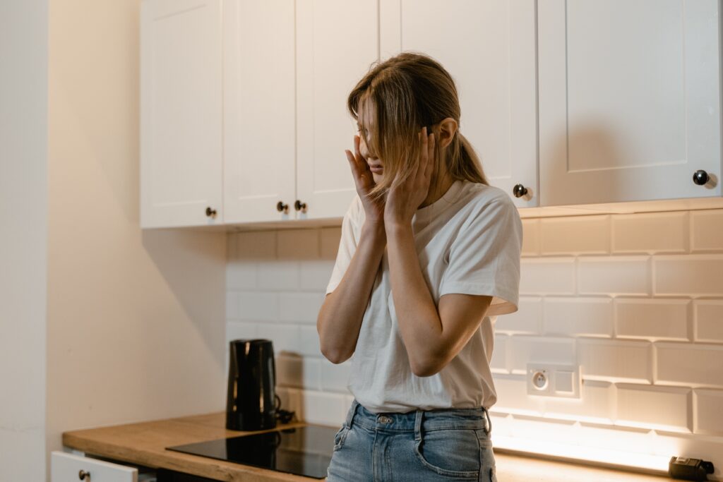 A woman standing in the kitchen with her hands to her face, depicting the Percocet side effects after abusing the drug