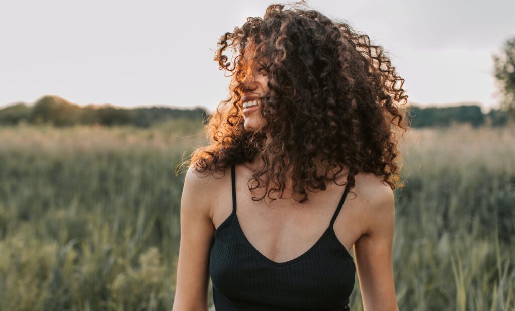 Woman walking through a grass field and smiling to represent inpatient mental health treatment